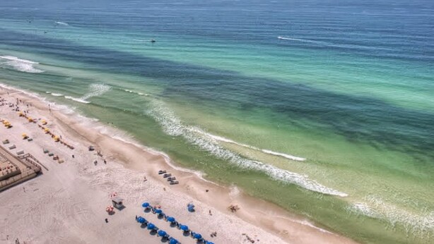 A beach with rows of umbrellas and sun loungers, a sandy shore, and the ocean. - Dunes of Panama 2 Bedroom Apartment (Panama City Beach)