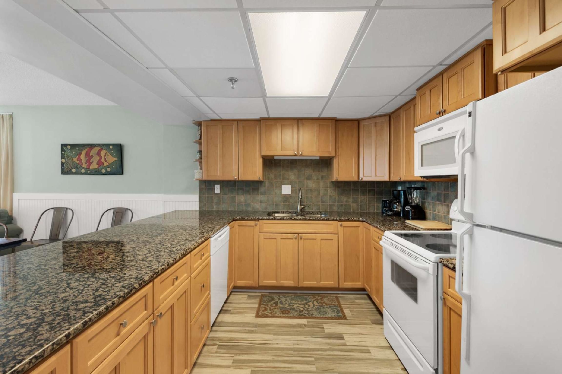 A kitchen with wooden cabinets, a granite countertop, a microwave, an oven, and a dishwasher.
