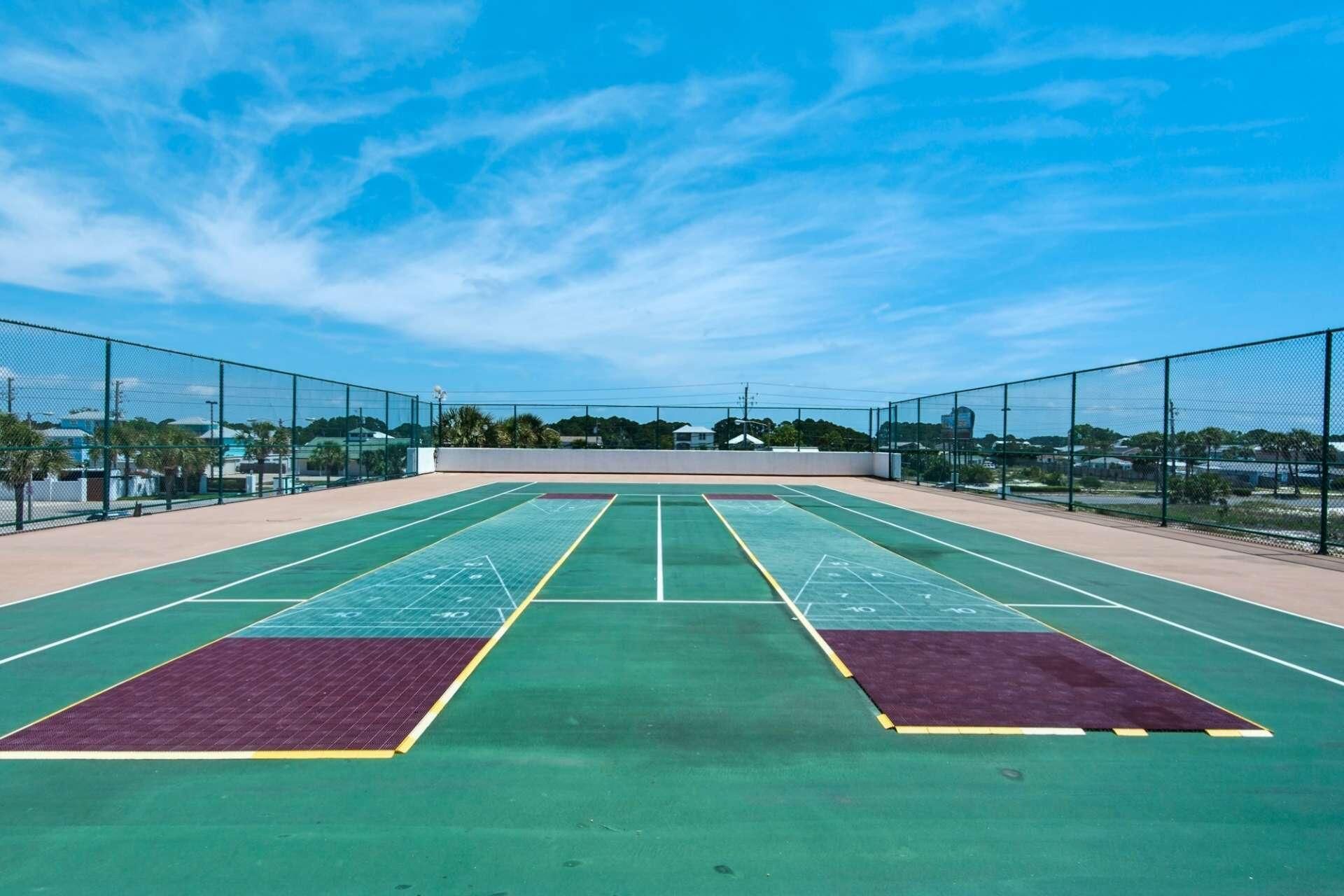 Un court de tennis en plein air, doté d’un filet et entouré d’une clôture, avec un ciel dégagé au-dessus.