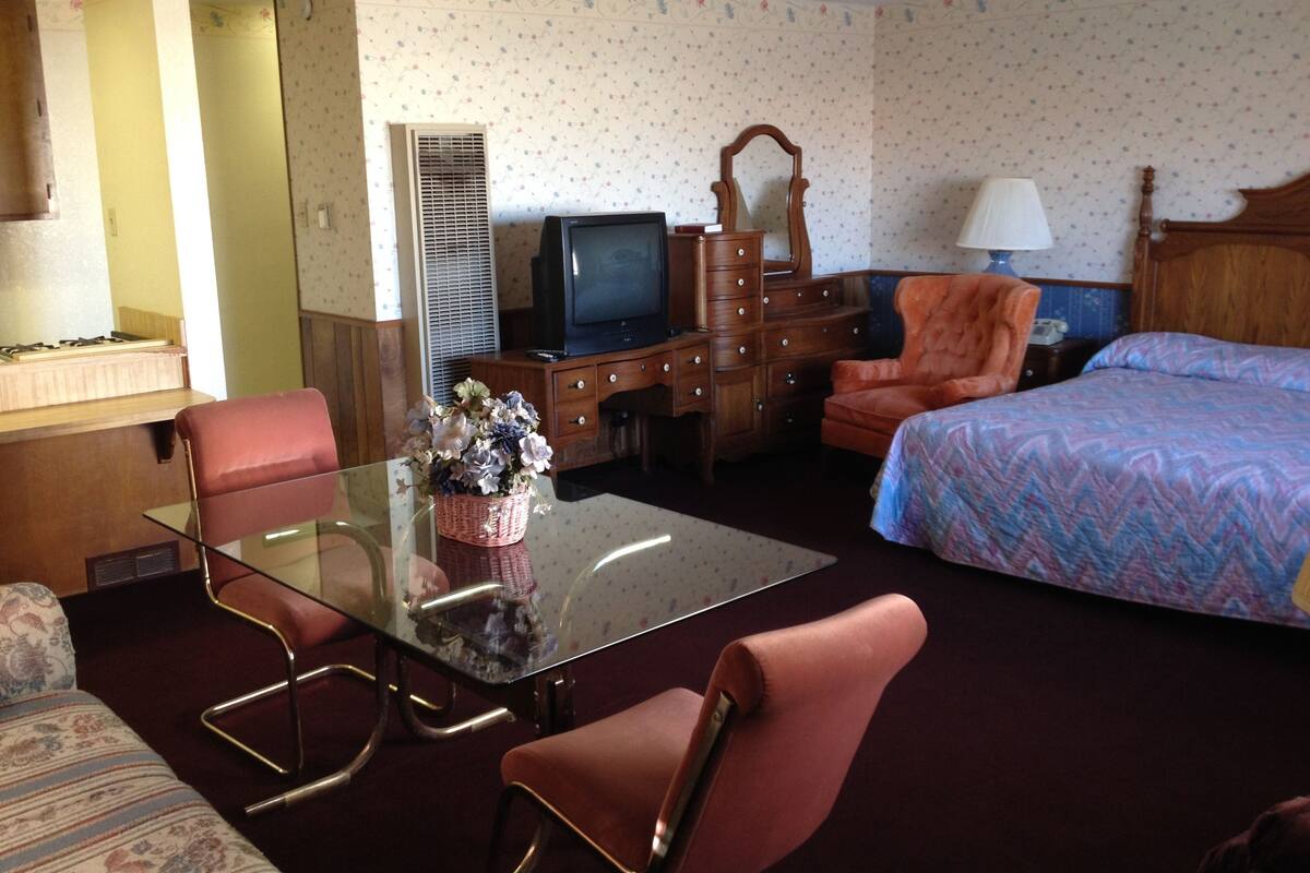 Une chambre d’hôtel comprenant un lit, un bureau, une chaise, une télévision, une commode et une lampe.