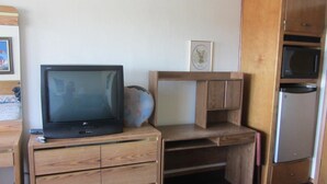 Una habitación compacta con escritorio de madera, televisor, microondas y refrigerador.