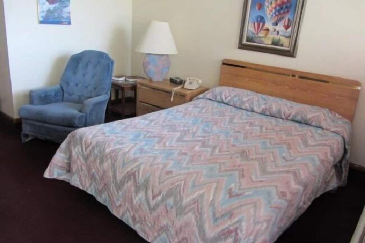 Une chambre d’hôtel comprenant un lit, une chaise, une table de chevet, une lampe et deux éléments de décoration murale.