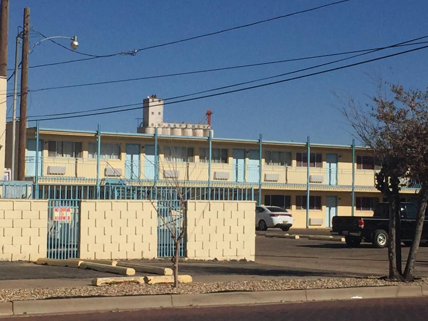 Un edificio de varios pisos con techo plano, una zona de estacionamiento cercada y un cielo azul despejado.