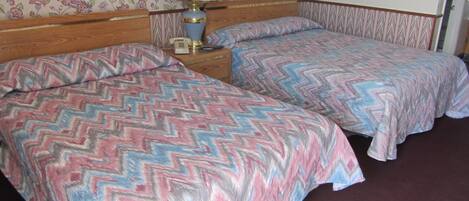 A room with two beds, each with a zigzag patterned bedspread, a nightstand with a lamp, and a floral wallpaper.