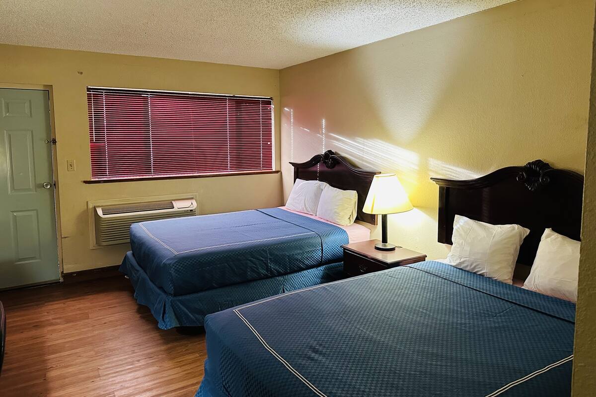 Une chambre d’hôtel avec deux lits, une fenêtre avec des stores, une lampe de chevet et une porte.