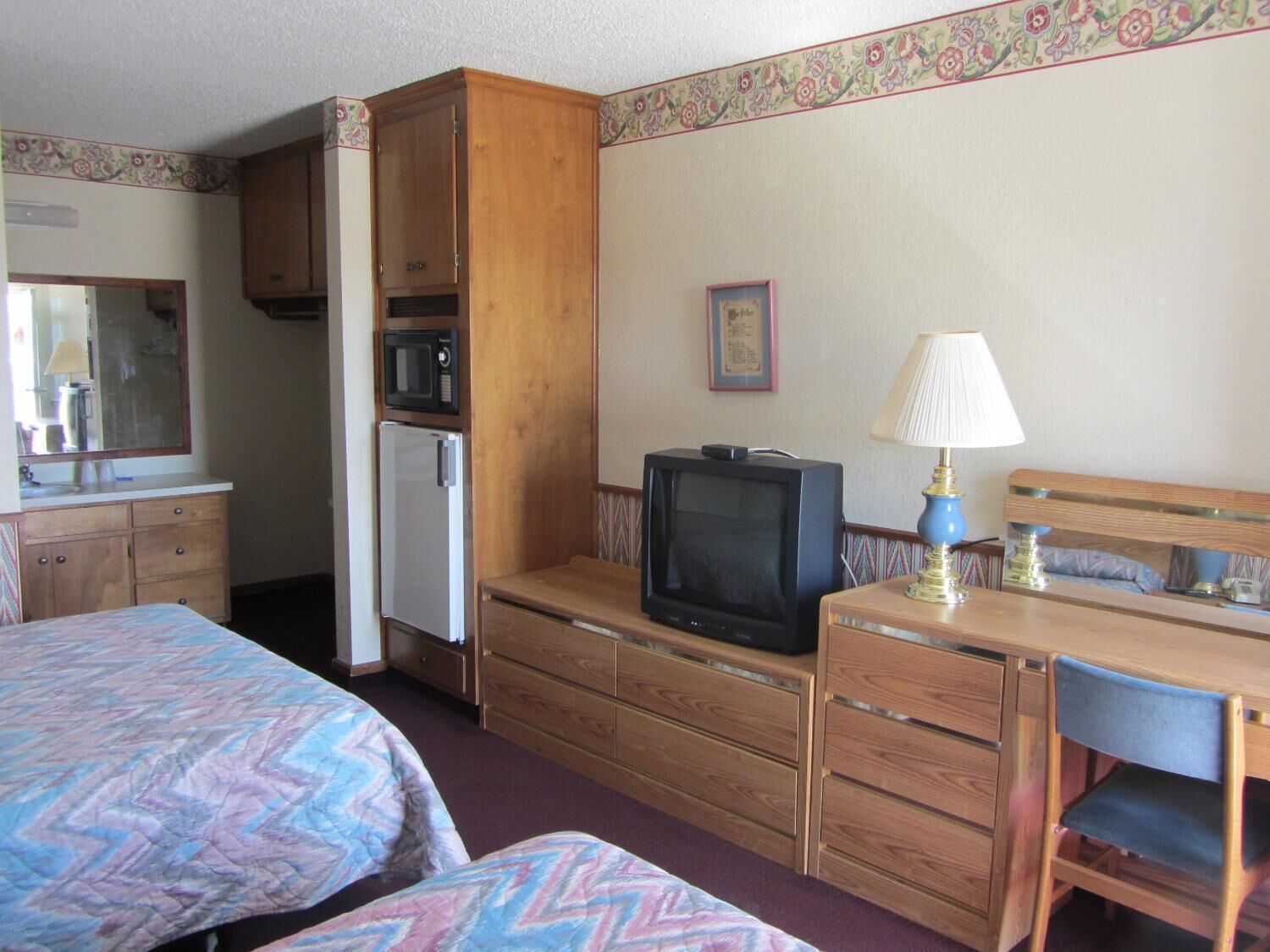 A compact hotel room with two beds, a small desk, a television, a microwave, and a refrigerator.