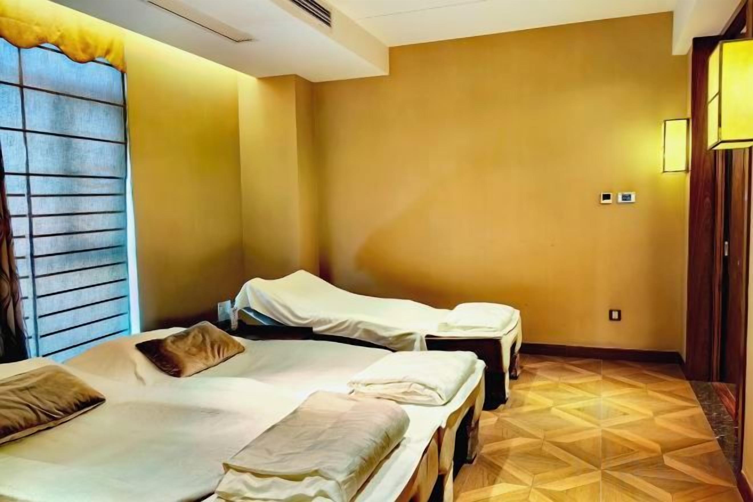 Une chambre d’hôtel avec deux lits, une fenêtre avec des stores, un plancher en bois et un luminaire fixé au mur.