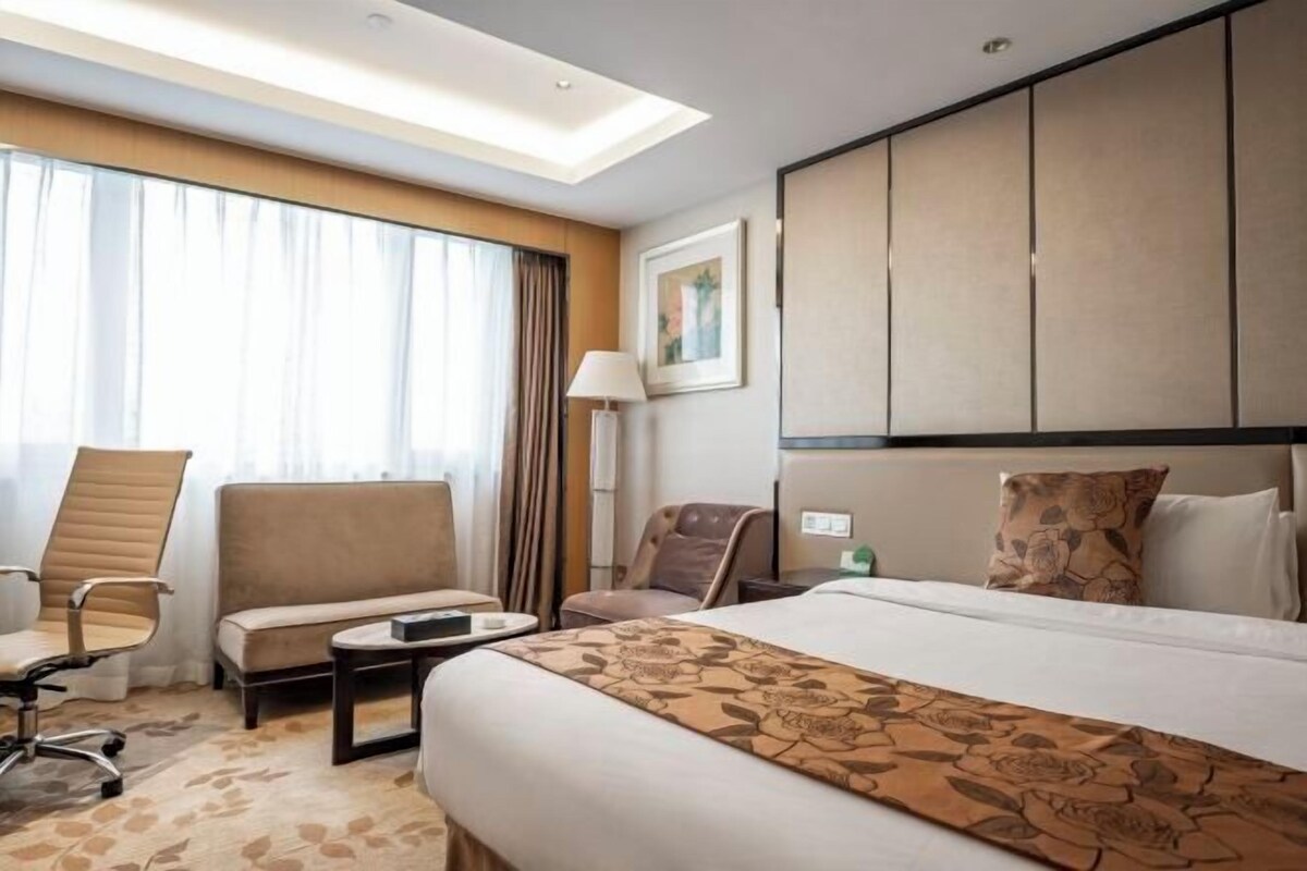 A hotel room with a large bed, a desk, a chair, and a sofa.