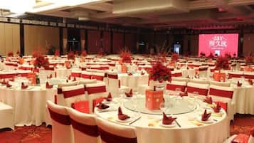 A banquet hall with round tables, red and white decor, and a stage with a pink screen.