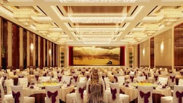 A banquet hall with rows of round tables, each with a white tablecloth and a purple bow.