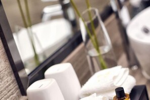A bathroom with a mirror, white towels, a bottle, and a glass. - Jiangyin Furen Boutique Hotel (Zhongshan Park Subway Station) (Jiangyin)
