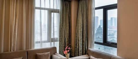 Una sala de estar moderna con un conjunto de sofá, un florero con flores y vista a la ciudad a través de amplias ventanas.