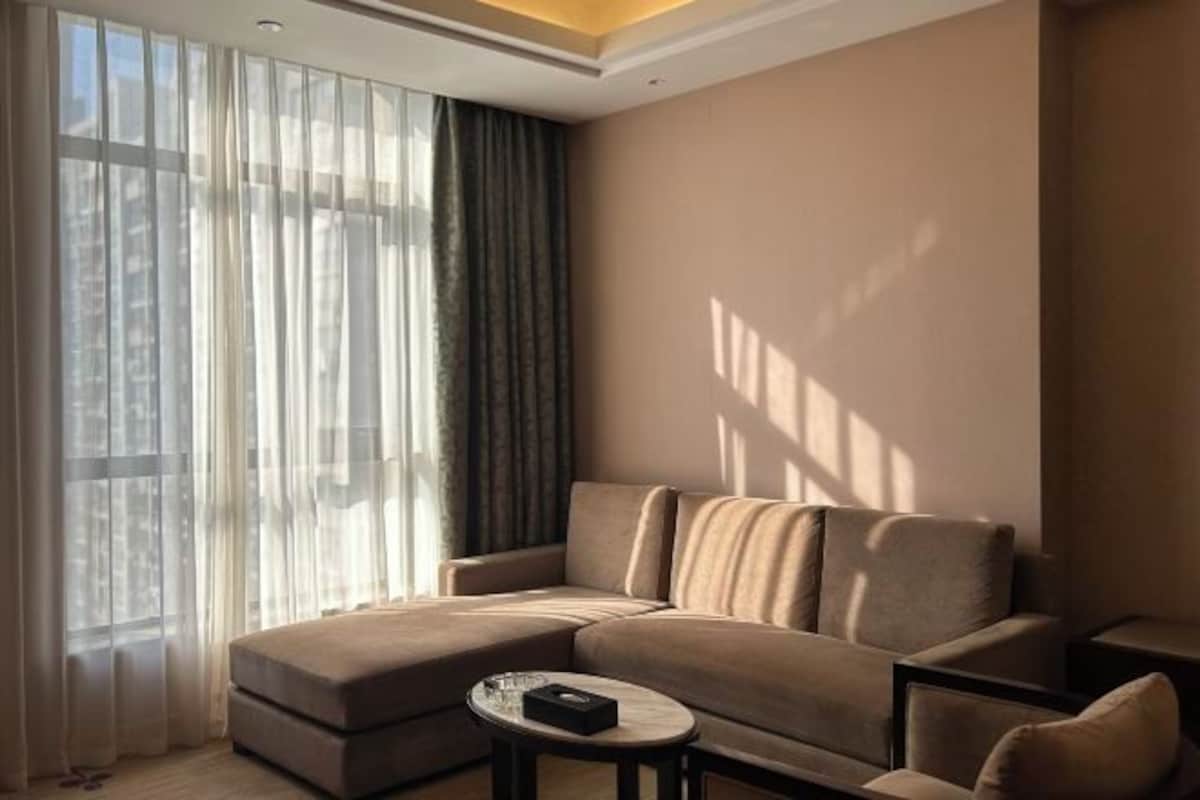A modern living room with a sectional sofa, a small round table, and sheer curtains on a large window.