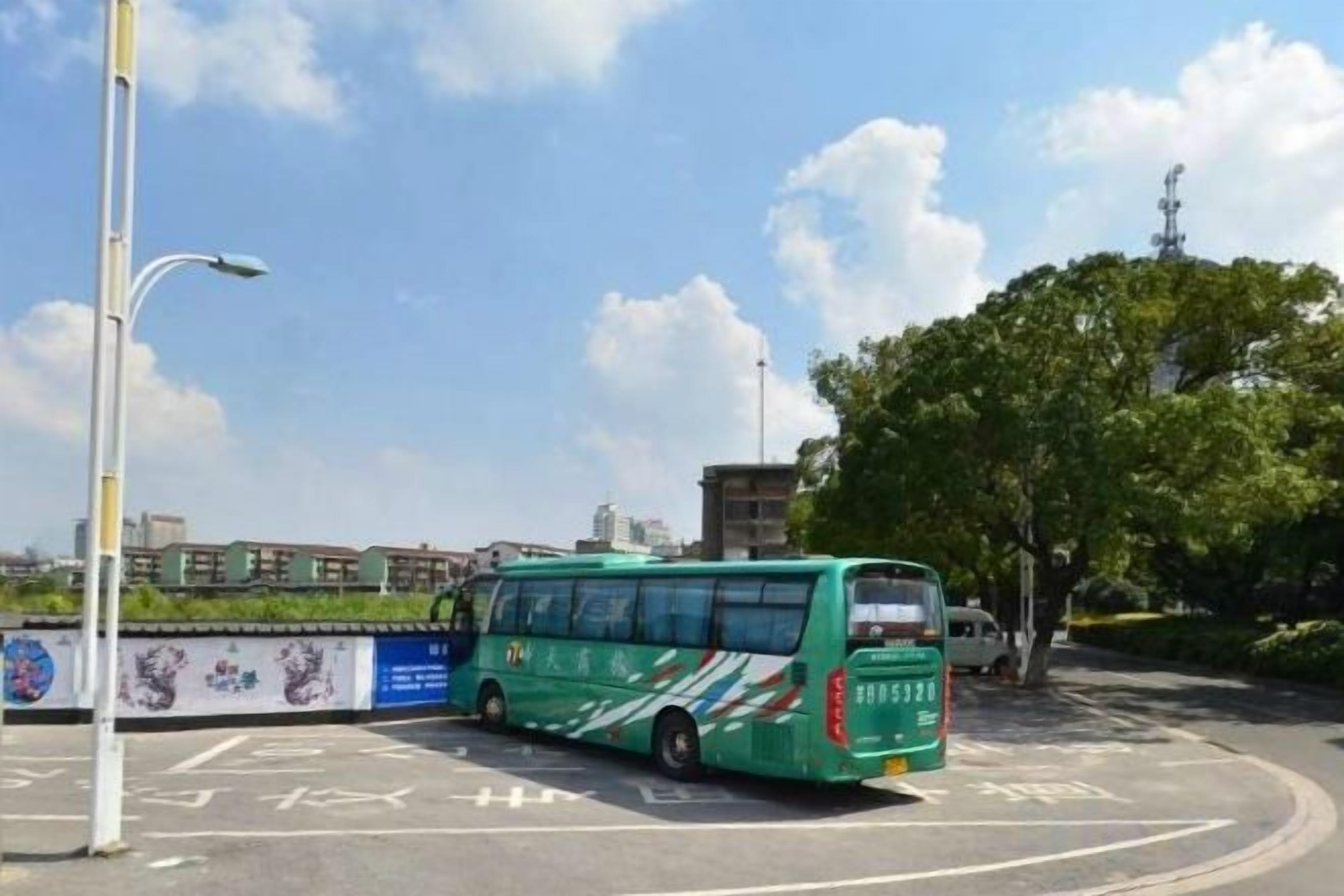 A green bus parked in a designated bus stop area with a clear sky and buildings in the background.