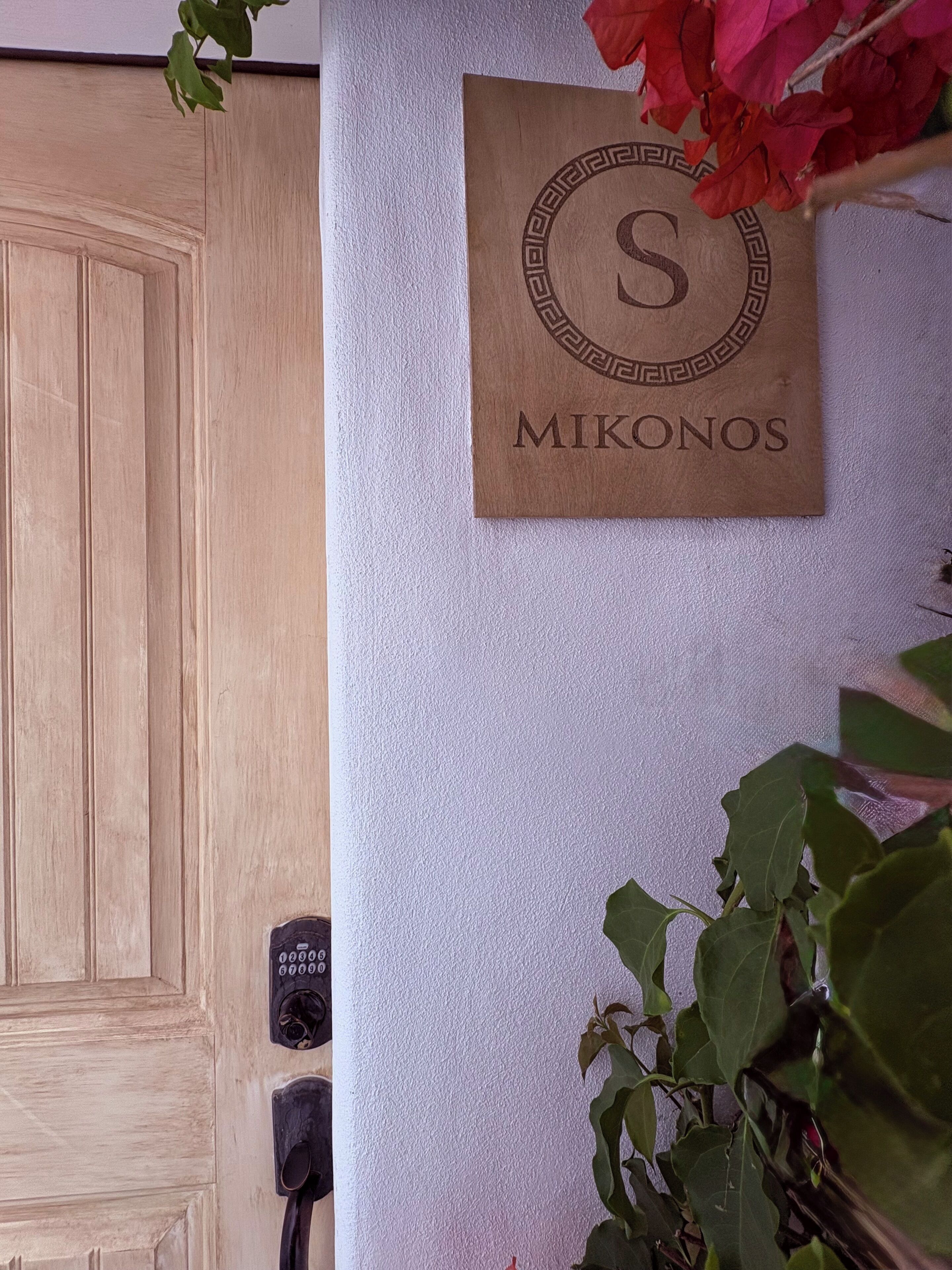 Eine Holztür, ein an der Wand befestigtes Schild mit Monogramm und Namen sowie ein Wandintercom.