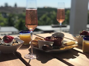 A table with breakfast items including a bowl of cereal with strawberries, a glass of orange juice, a glass of rosé wine, a plate with pastries, and a bowl of yogurt with blueberries. - Sirena Resort (Paso Robles)