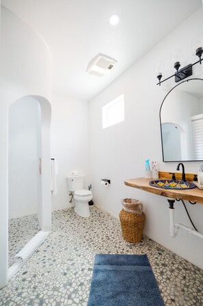 A bathroom with a white toilet, a sink with a decorative basin, a mirror, and a tiled floor. - Sirena Resort (Paso Robles)