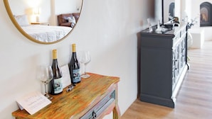 A room with a round mirror, a wooden console table with wine bottles and glasses, a dark cabinet, and a television. - Sirena Resort (Paso Robles)