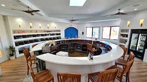 A bar area with a curved counter, wooden chairs, and shelves of bottles. - Sirena Resort (Paso Robles)