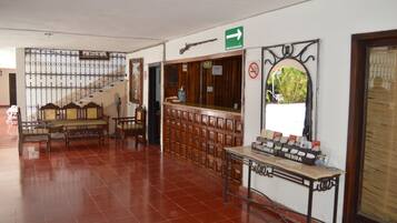 Vestíbulo con una escalera, bancos de madera, un mostrador de recepción y un letrero en la pared que indica una salida.