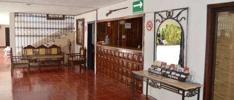 Vestíbulo con una escalera, bancos de madera, un mostrador de recepción y un letrero en la pared que indica una salida.