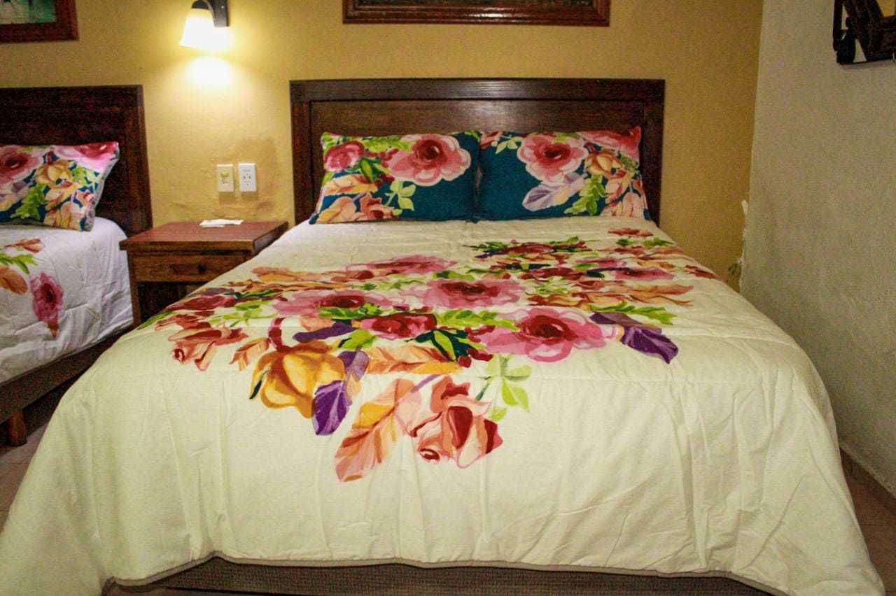 A hotel room with a large bed, a nightstand, and a wall-mounted lamp.