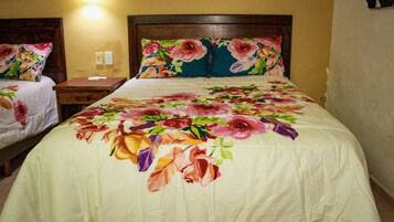 A hotel room with a large bed, a nightstand, and a wall-mounted lamp.