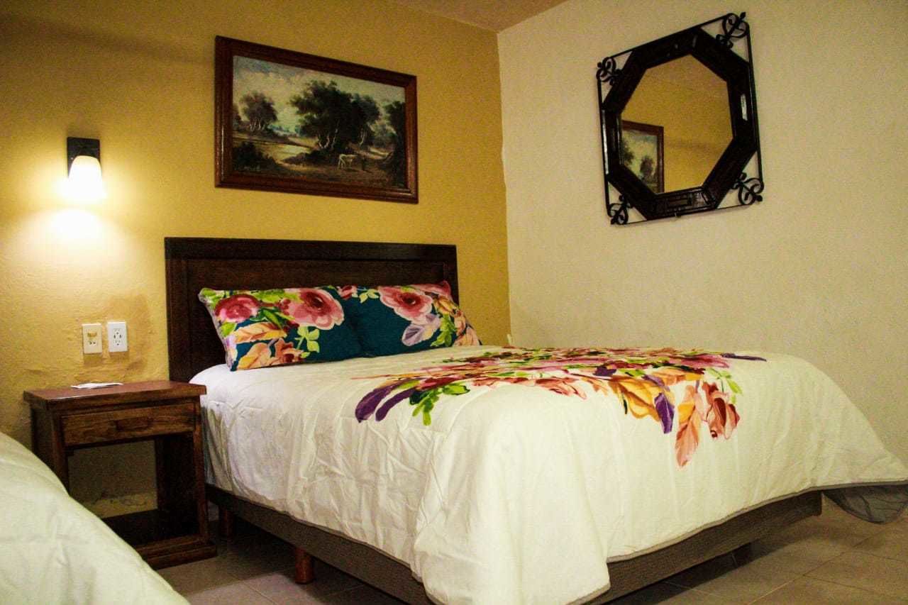 A bedroom with a bed, a nightstand, a wall-mounted mirror, and a painting above the bed.