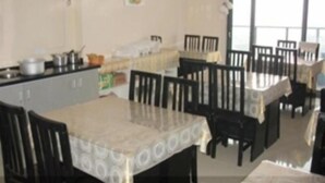 A dining area with a table set for four, surrounded by chairs. There is a kitchen area with cabinets and a stove in the background. - Greentree Inn (Xuzhou)