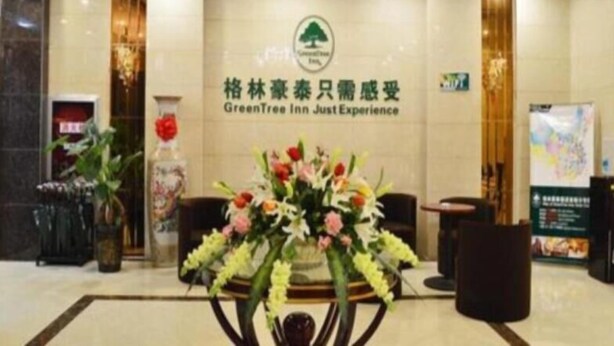 A reception area with a chandelier, a floral arrangement, and a wall with the GreenTree Inn logo. - Greentree Inn (Xuzhou)
