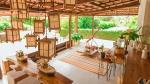 Un intérieur en bois agrémenté de lanternes suspendues, un coin repas avec une table et des chaises, et une vue sur la verdure à l’extérieur.