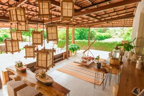 Een ruim terras met houten meubels, hanglampen en potplanten.