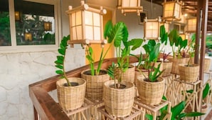 A room with wicker planters on a wooden table, bamboo lanterns hanging from the ceiling, and a window with a view of greenery. - Ecocharme Pousada Do Marcilio (Fernando de Noronha)