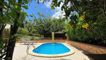 A rectangular swimming pool with a ladder, surrounded by a brick border, under a tree canopy.
