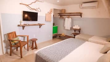 A hotel room with a bed, a chair, a small table, a TV, and a shelf with towels and a basket.