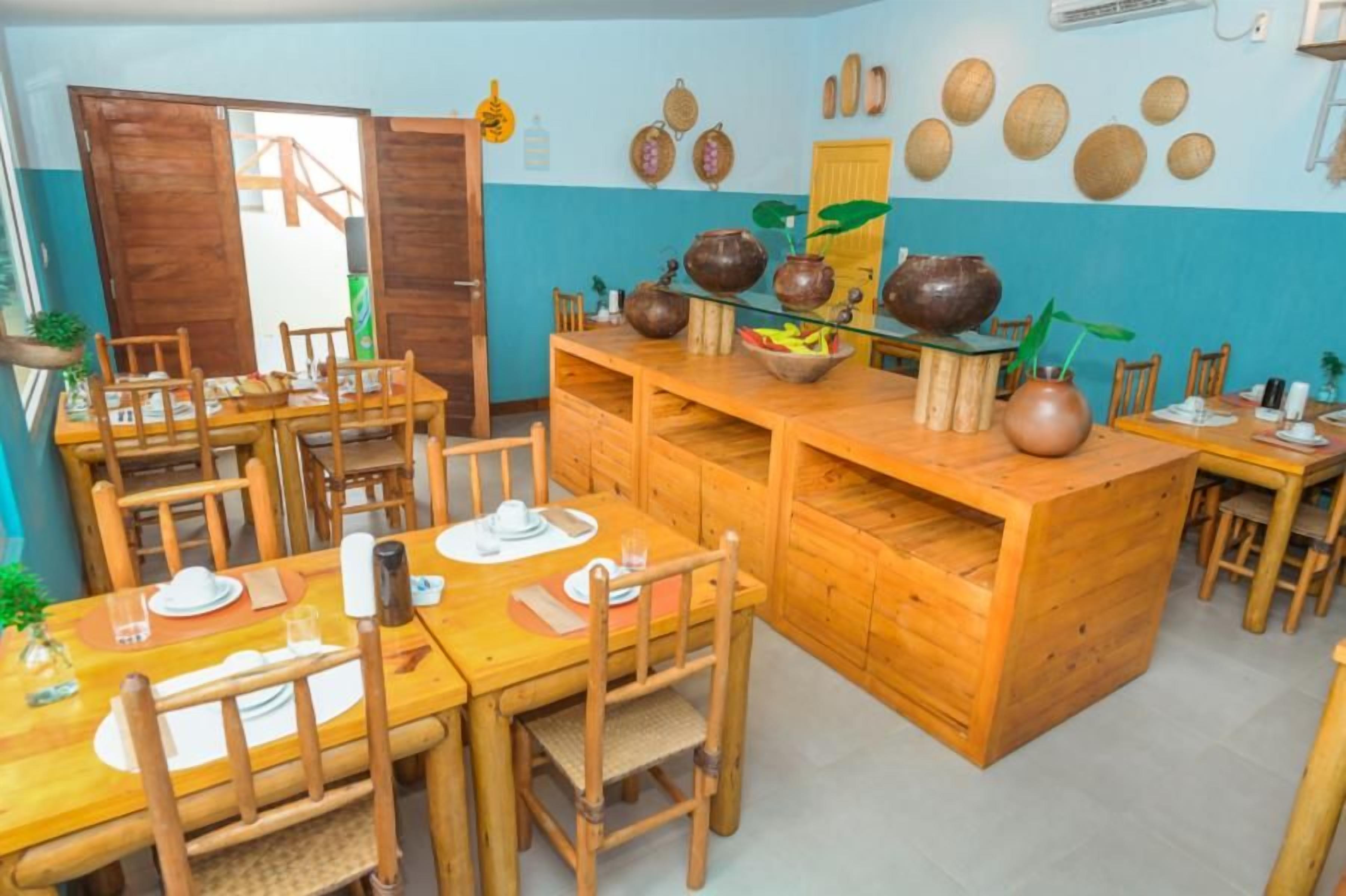 A dining area with wooden tables and chairs, a central island with pottery, and a wall decorated with woven baskets.
