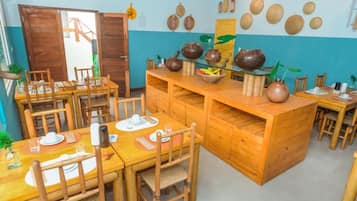 A dining area with wooden tables and chairs, a central island with pottery, and a wall decorated with woven baskets.