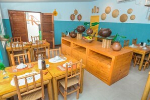Un espace repas avec des tables et des chaises en bois, un îlot central orné de poteries et un mur décoré de paniers tressés.