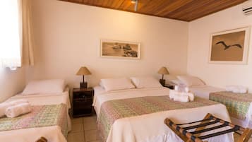 A room with two beds, each with a floral bedspread, a wooden chair, a nightstand with a lamp, and a painting on the wall.