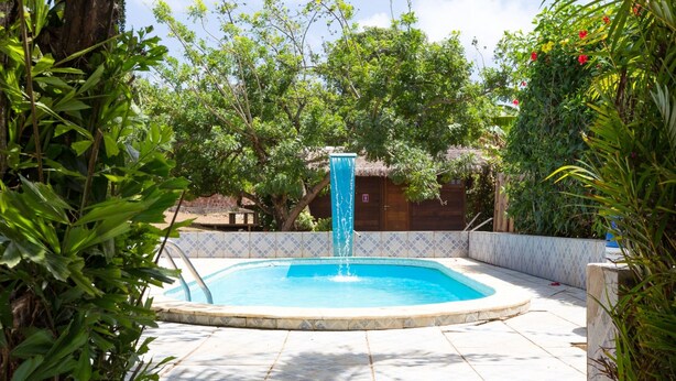 Une piscine avec une fontaine, entourée d’une végétation luxuriante et dotée d’une terrasse carrelée.