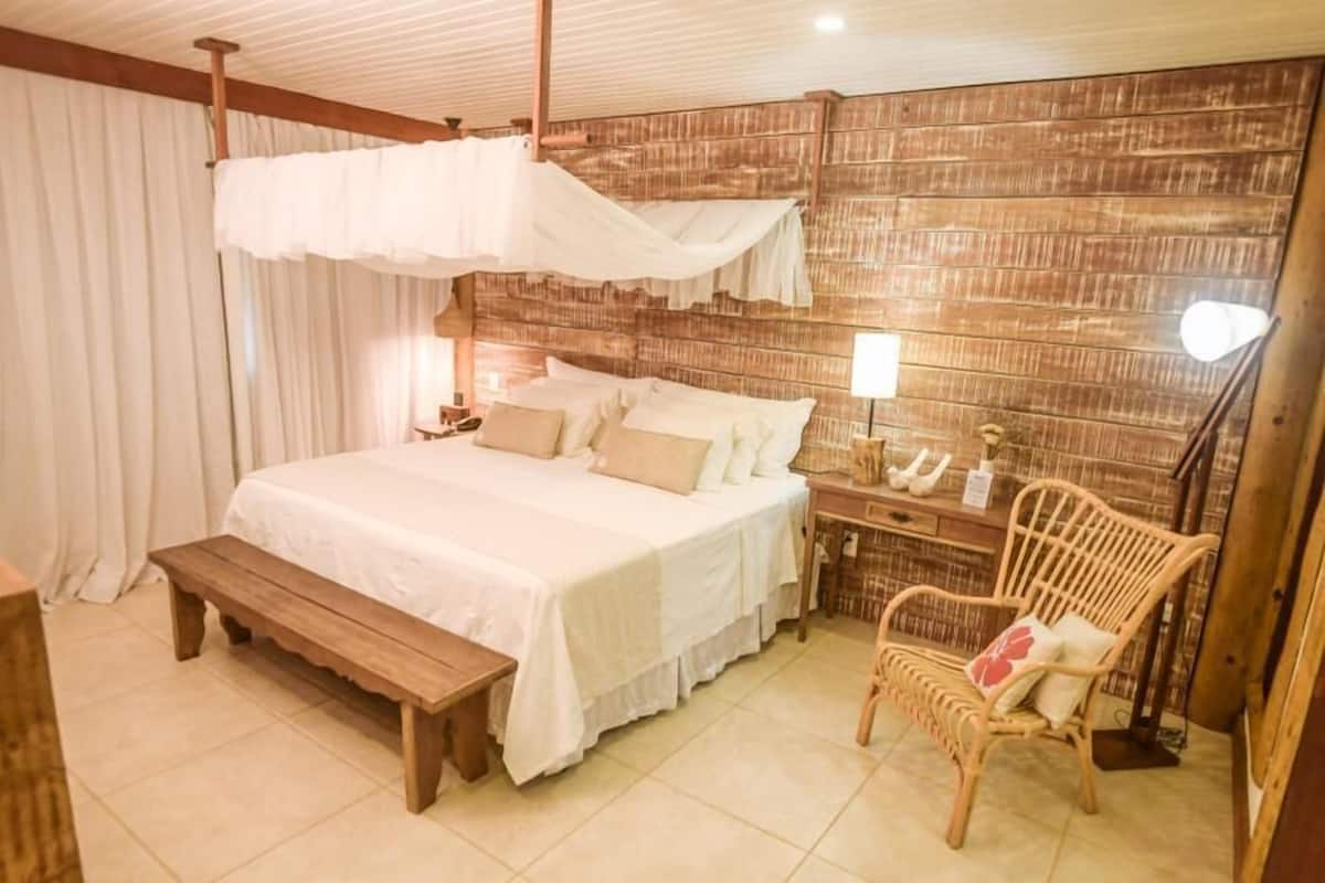 A bedroom with a large bed, a bench, a chair, and a wooden wall.