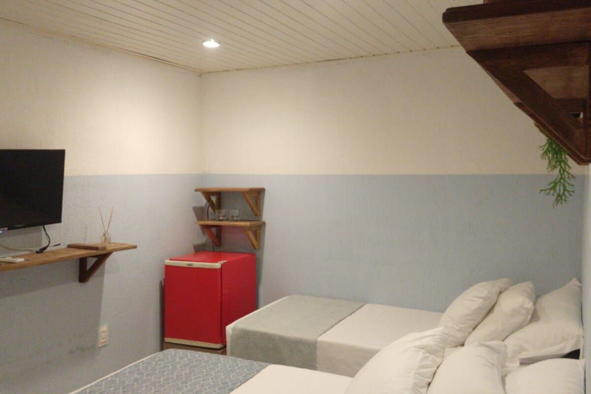 Une pièce avec un lit, une télévision, une armoire rouge et une étagère.