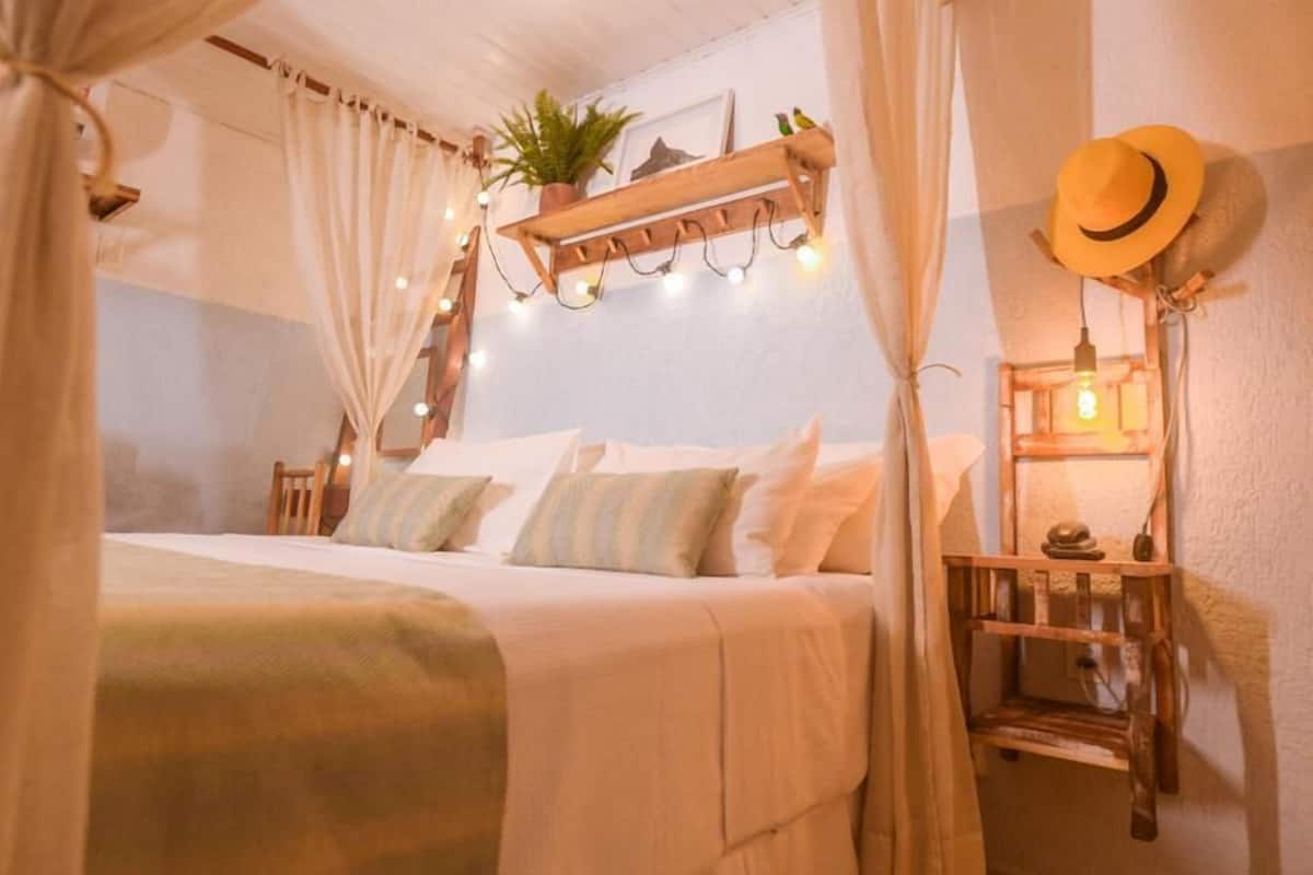 A cozy bedroom with a bed, curtains, a shelf with lights, a hat, and a plant.