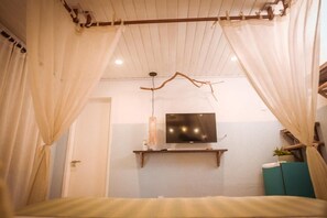 Une chambre à coucher avec un lit, un téléviseur fixé au mur et une petite étagère sur laquelle se trouve une plante.