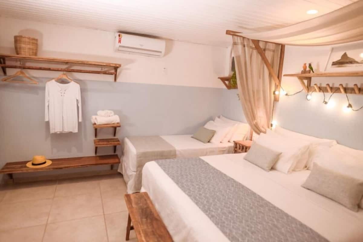 Un dormitorio con dos camas, un banco, una cesta colgante y un estante con toallas.