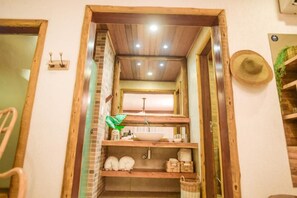 Een smalle badkamer met houten kozijnen, een wastafel, planken en een hangende hoed.