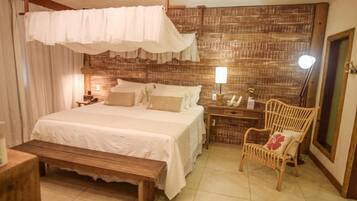 A bedroom with a large bed, a wooden bench, a wicker chair, and a nightstand with a lamp.