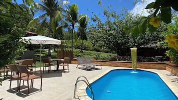 Una piscina con solárium empedrado, rodeada de sillones de descanso y una zona de estar cubierta.