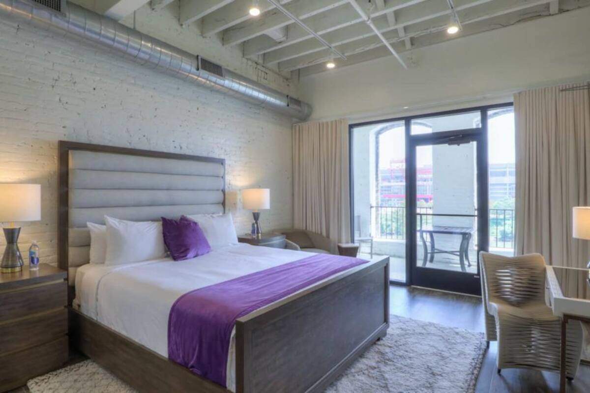 A modern hotel room with a large bed, a desk, and a balcony with a view.