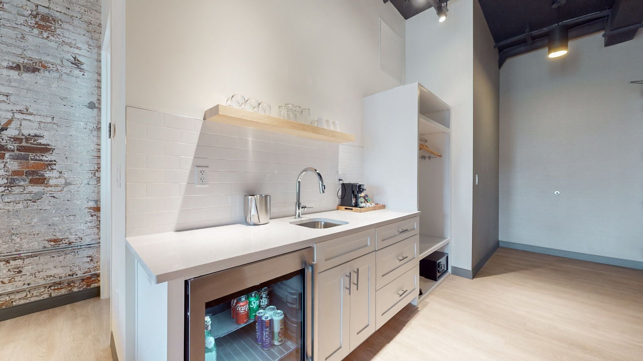 A modern kitchen with a white countertop, stainless steel sink, and wooden shelves.